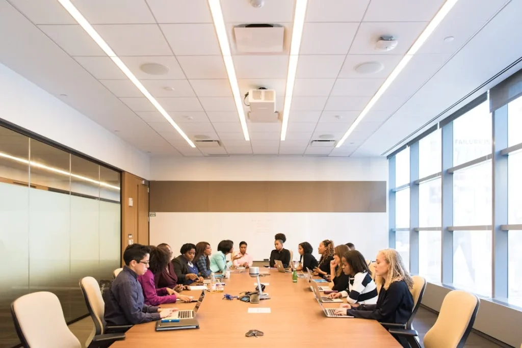 A group of people working around a large board room table. You can tell they want to get out and have some fun.